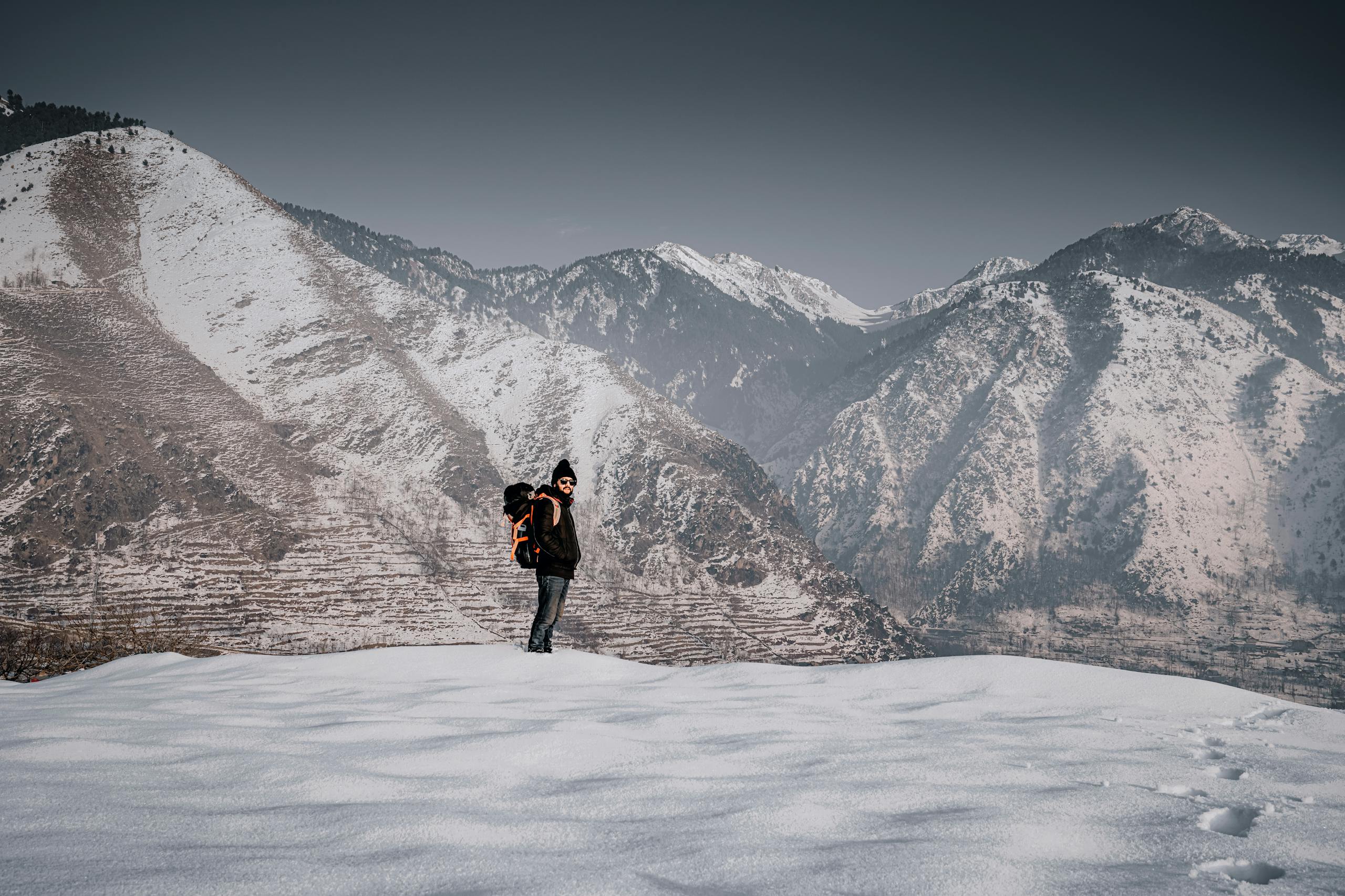 A backpacker stands amidst snow-covered mountains in Kashmir, enjoying a serene winter landscape.