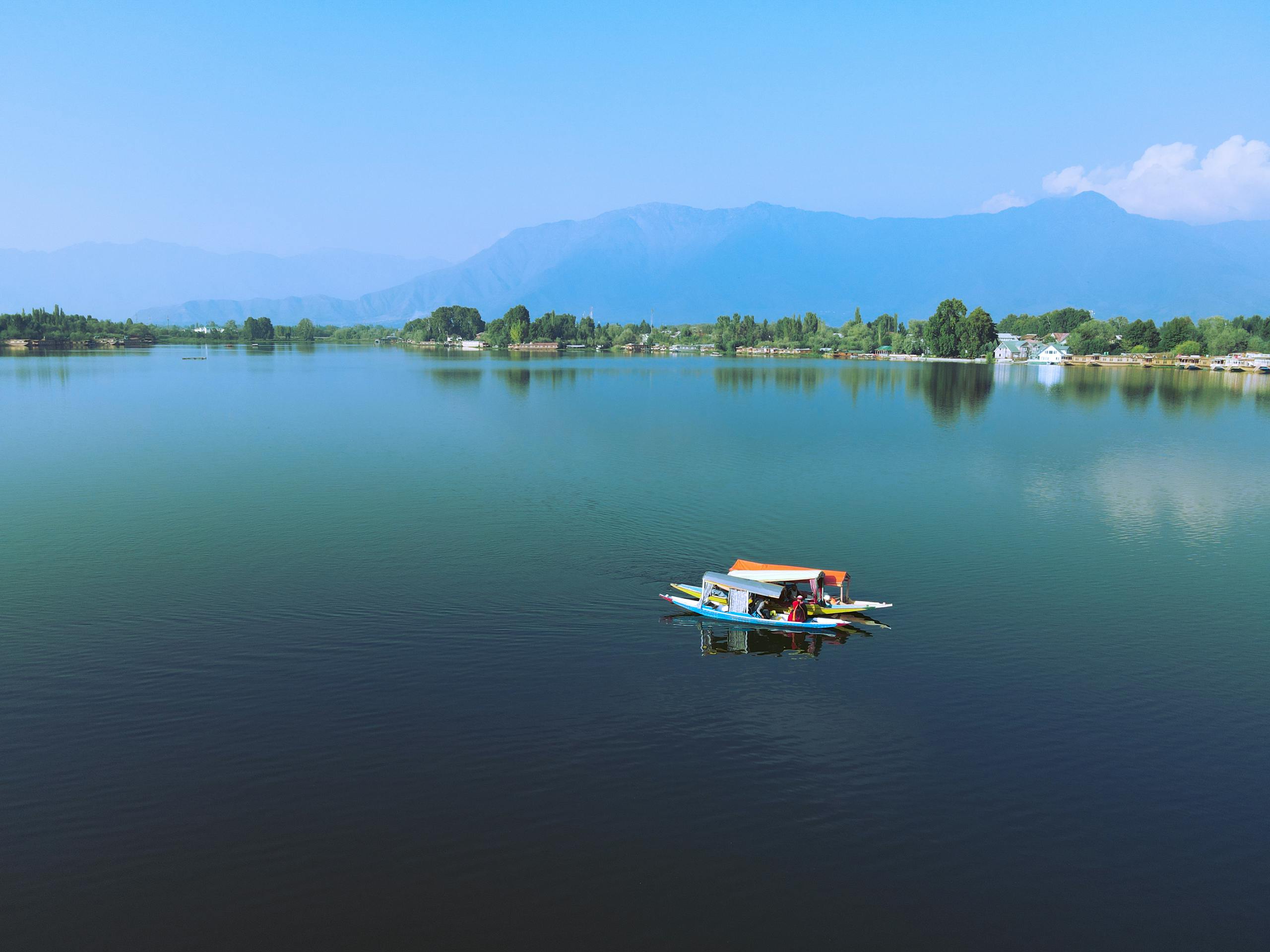 A peaceful scene of a shikara boat on Nigeen Lake in Kashmir with mountains in the background.