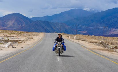 A solitary biker traveling through the rugged terrain of Leh, surrounded by majestic mountains.