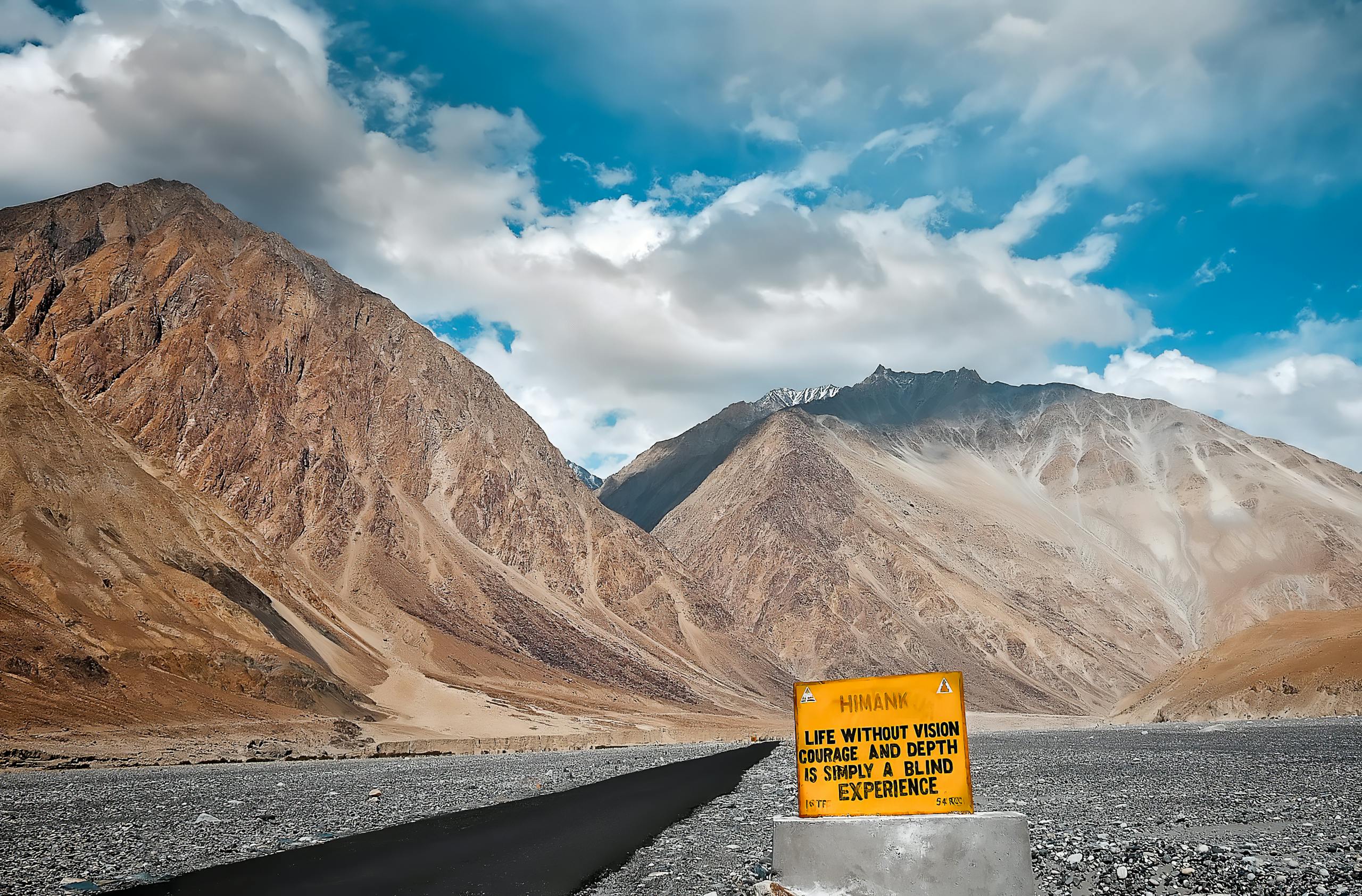 An inspiring view of a mountainous road with an encouraging road sign under a blue sky.
