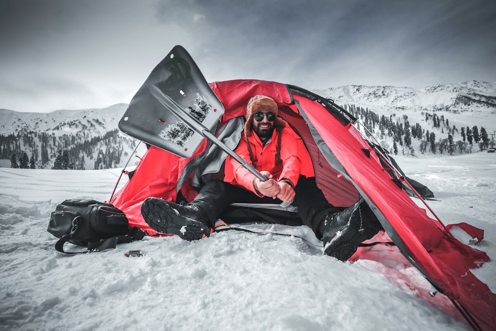Man shoveling snow outside a tent in the snowy mountains of Gulmarg. Winter camping adventure.