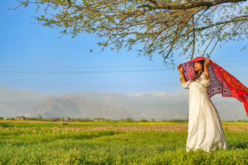 Woman in white dress and shawl stands peacefully under a tree in Kashmir.