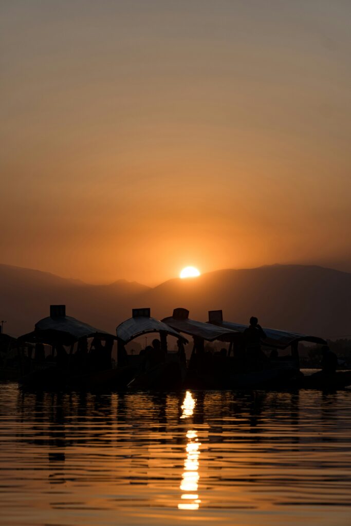 Silhouette of boats on Dal Lake in Srinagar against a golden sunset backdrop.