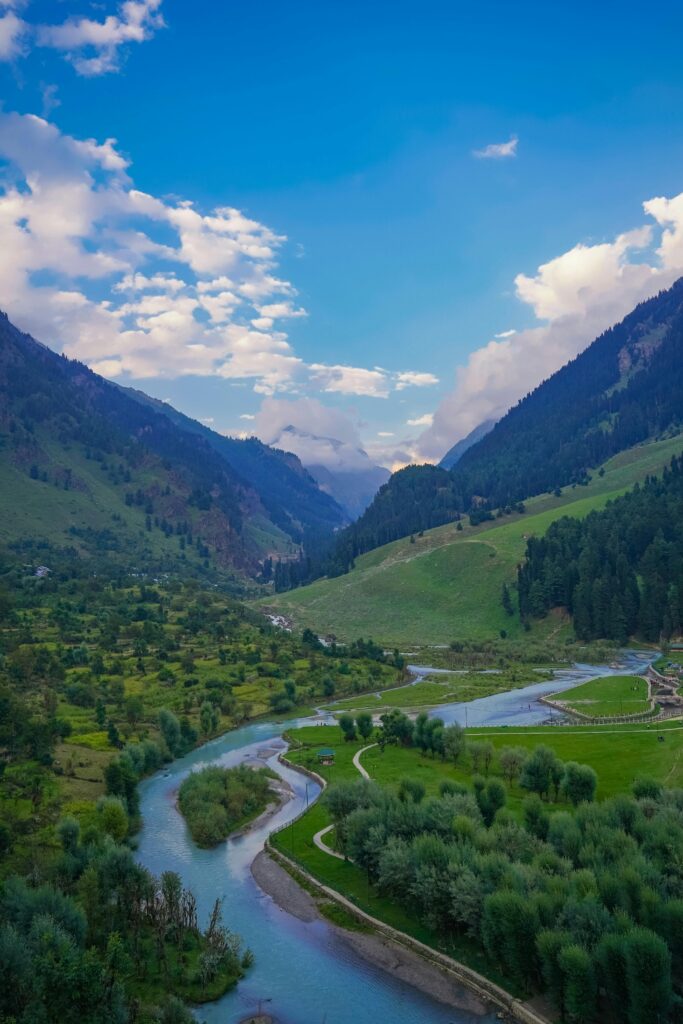 Breathtaking view of a lush valley with a winding river and majestic mountains under a bright blue sky.